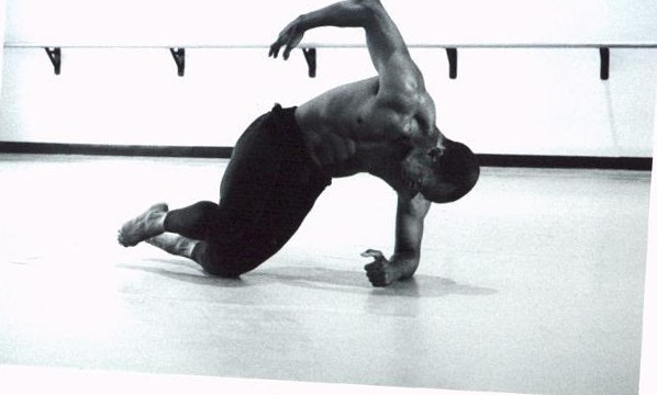 Black-and-white photograph of Boris Willis low to the floor in a crouching dance pose, one arm arcing overhead