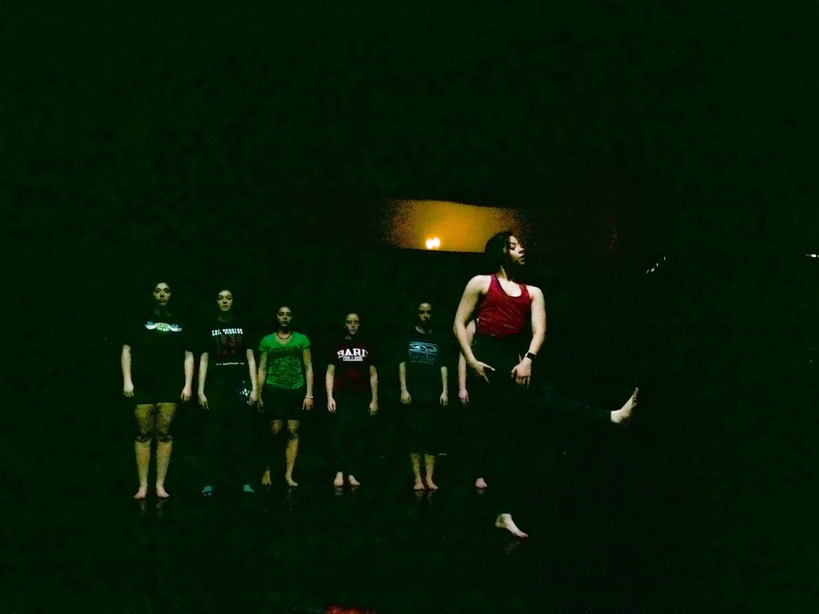 Dancers in a dim line as a soloist steps forward, a single warm light glowing behind them