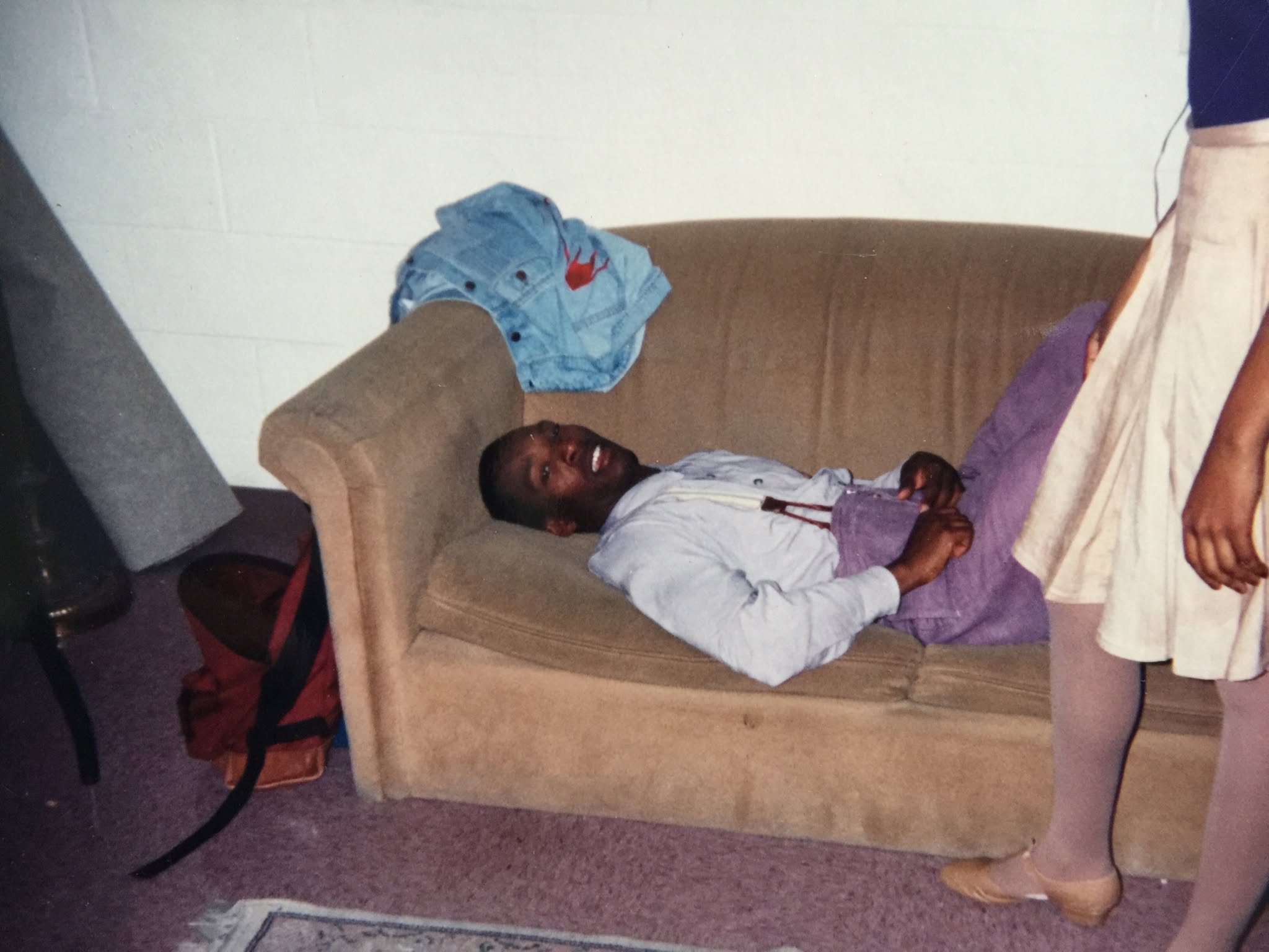 Boris Willis reclining on a couch backstage, a dancer in a white skirt standing beside him