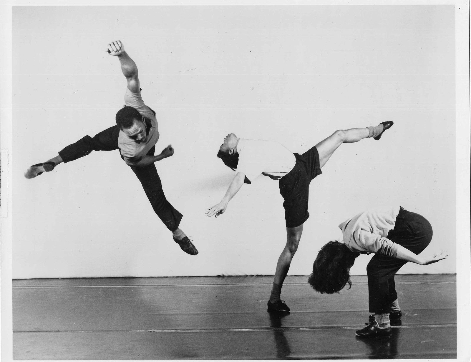 Vintage black-and-white performance photograph of three dancers in mid-movement, one leaping with arms flung wide