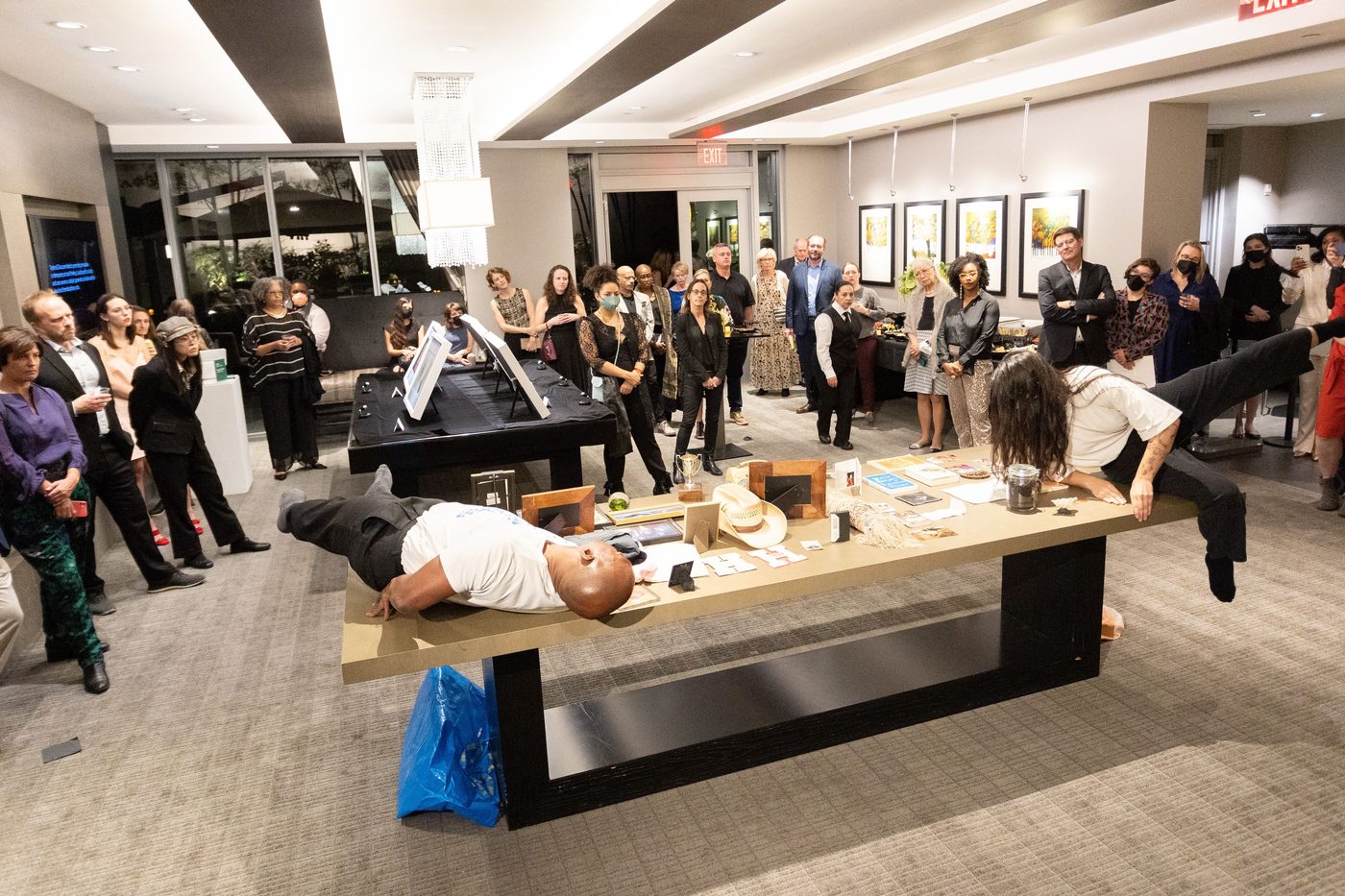 Boris Willis and Rex Delafkaran performing on a long table before a gallery audience